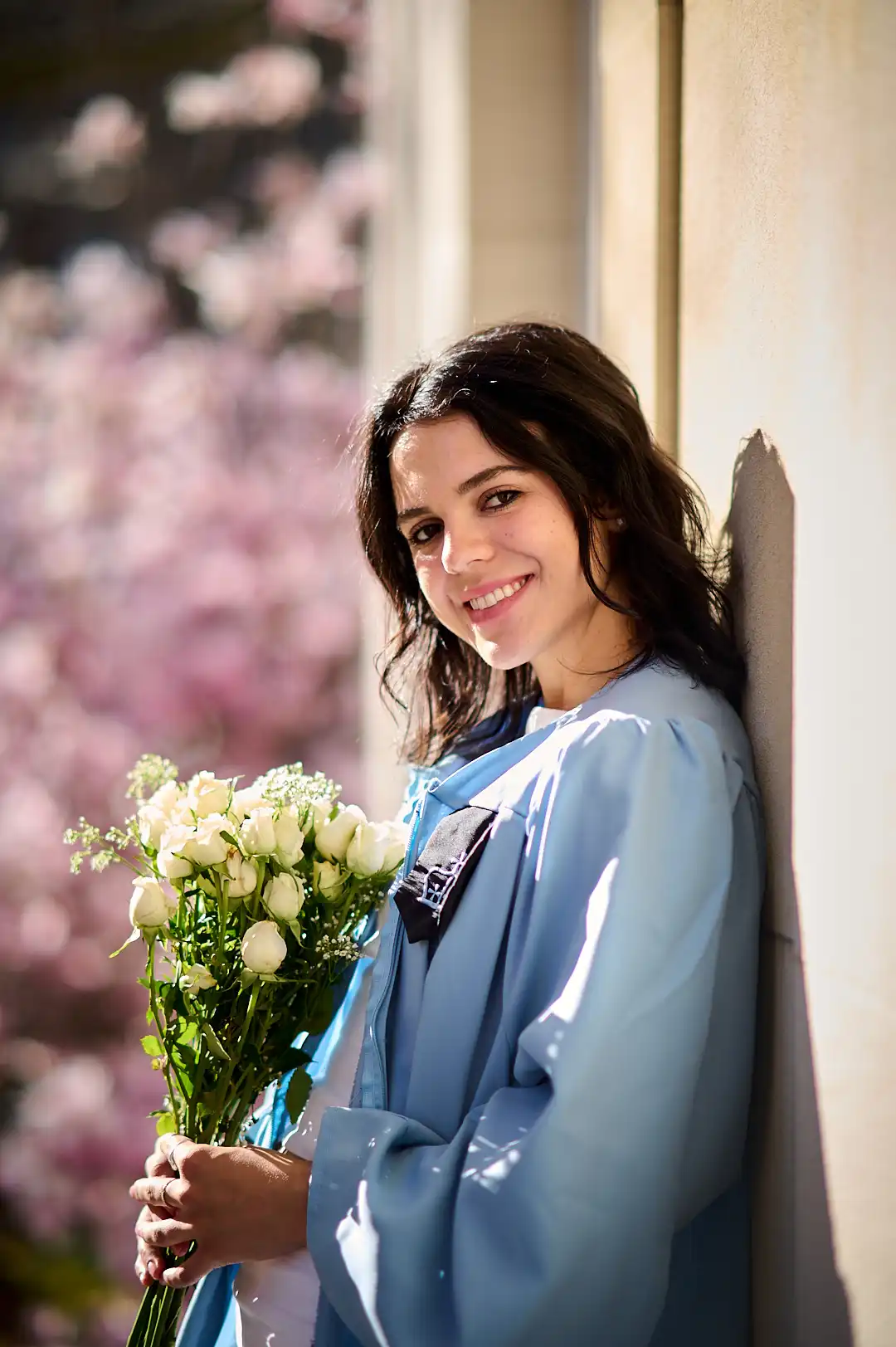 Graduate in light blue Columbia hood and navy dress, gothic brick building behind
