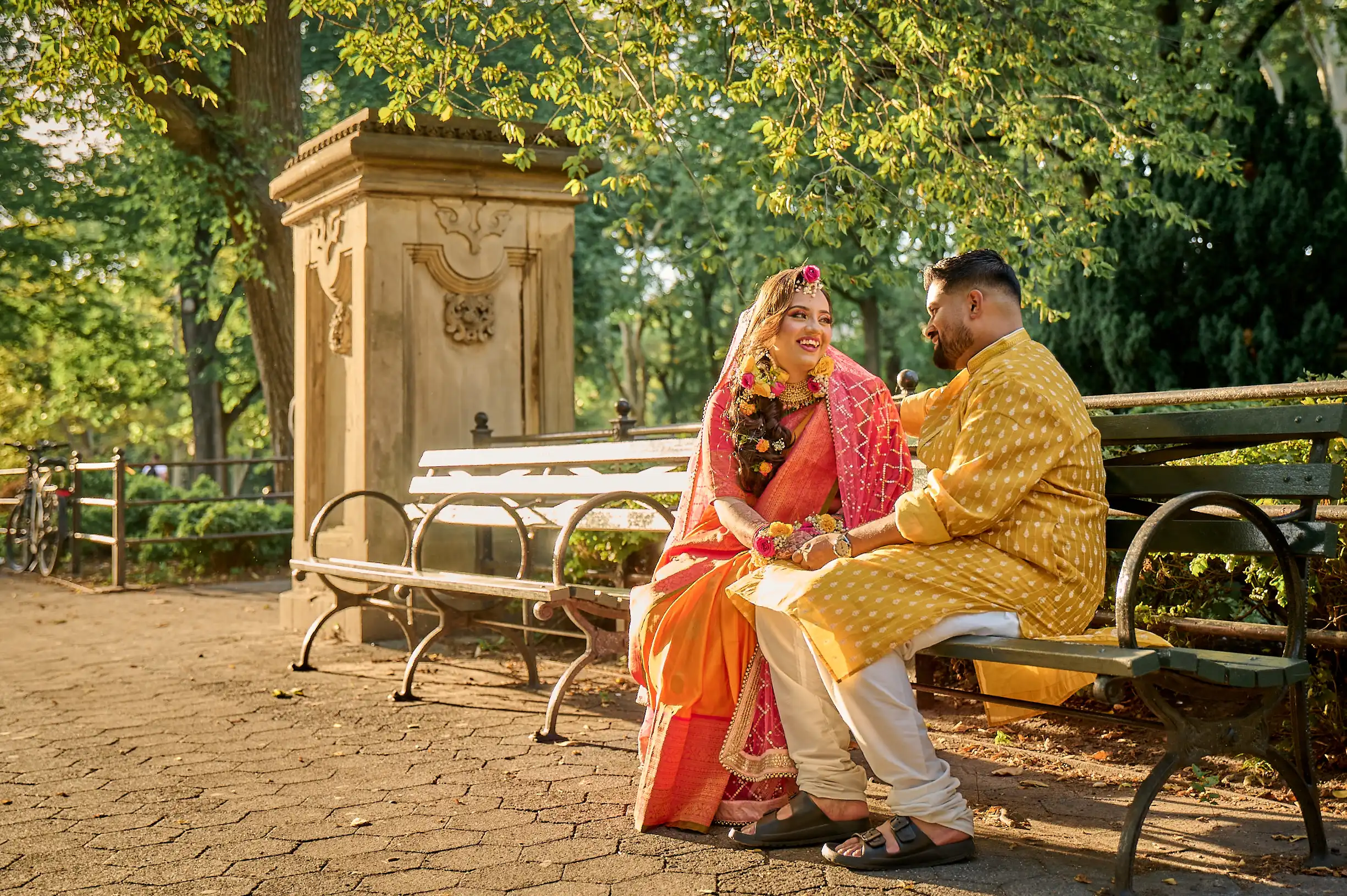 Bride in red bridal sari and groom in navy sherwani standing in front of huge brass-paneled doors